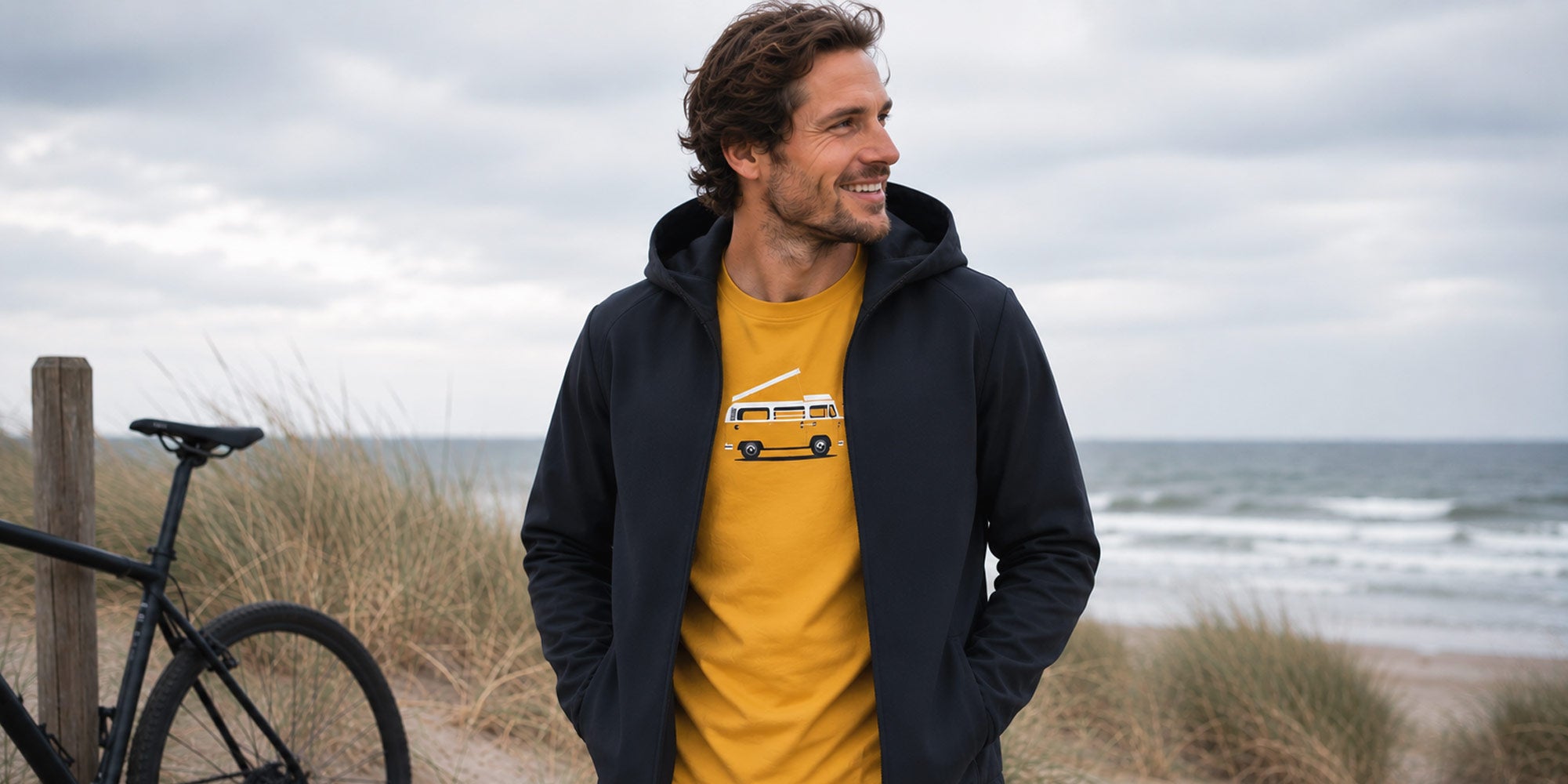 Mann am Strand mit Elkline Softshelljacke und Wheeldom Bulli T-Shirt