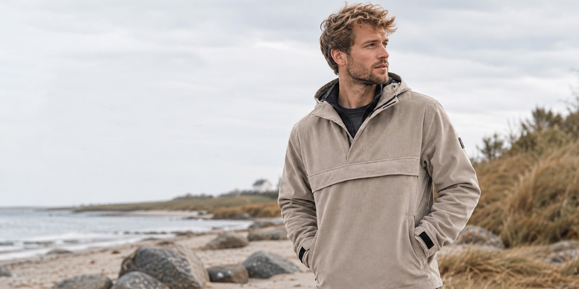 Mann am Strand trägt die Schlupfjacke SCHLUPF mit der feinen Cord Optik. Wasserdicht, winddicht, atmungsaktiv 