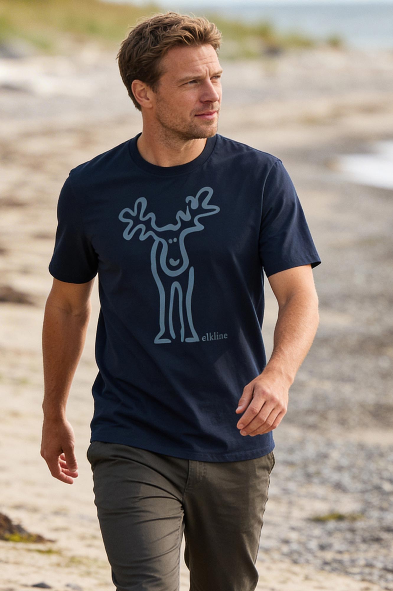 Mann geht am Strand spazieren. Er trägt das T-Shirt Rudolf in darkblue